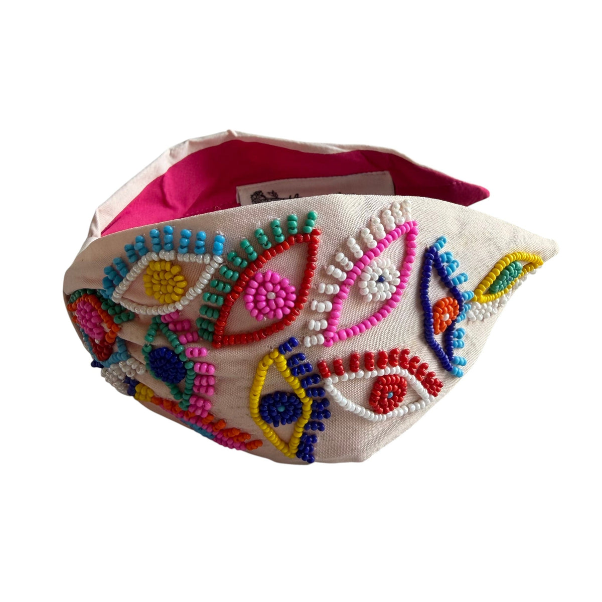 The Marigold Story white headband featuring vibrant multicolor seed bead evil eye motifs and a hot pink inner lining.