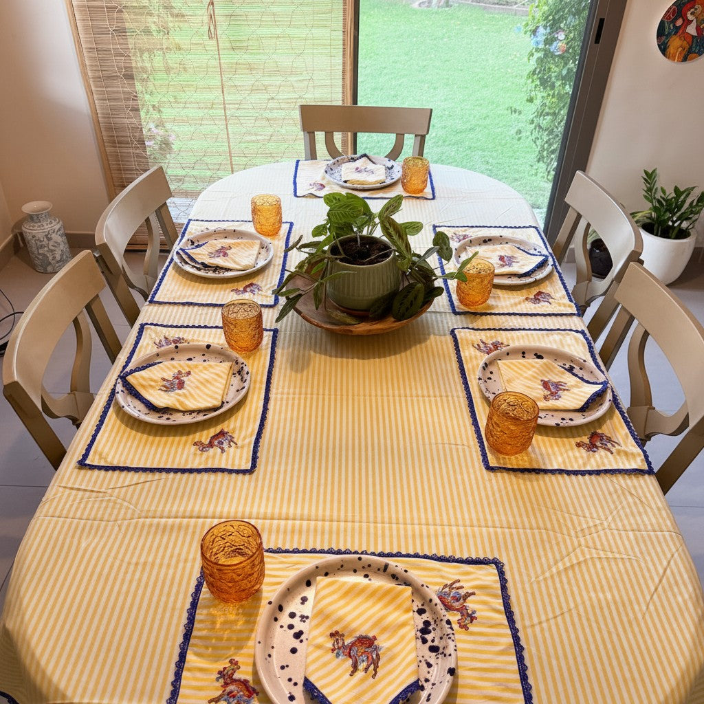 The Marigold Story yellow and white striped table linen set with camel embroidery and blue lace trim on a dining table