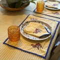The Marigold Story yellow and white striped table linen set with embroidered camel motifs and blue lace trim.