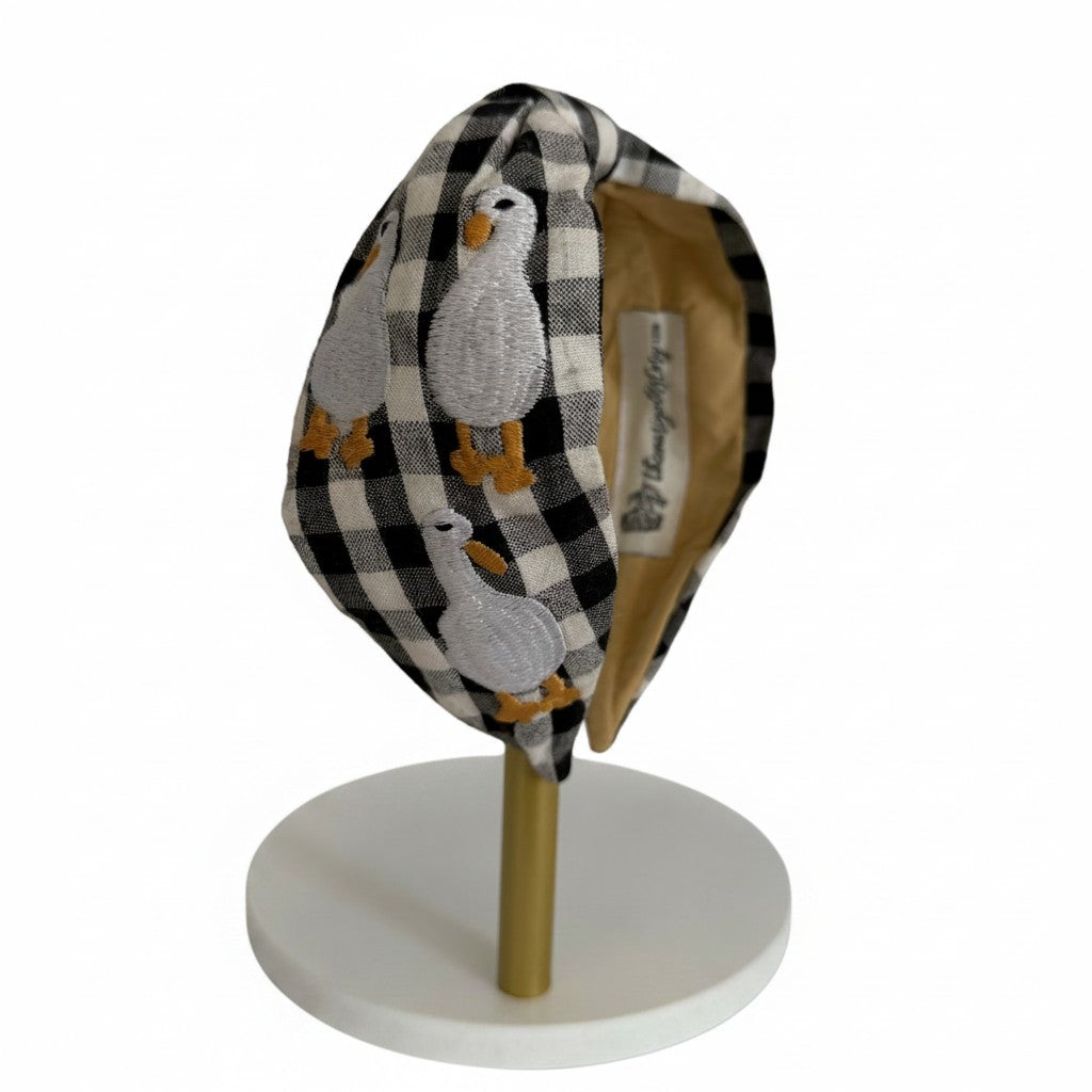 The Marigold Story black and white gingham headband featuring hand-embroidered white ducks with golden feet.
