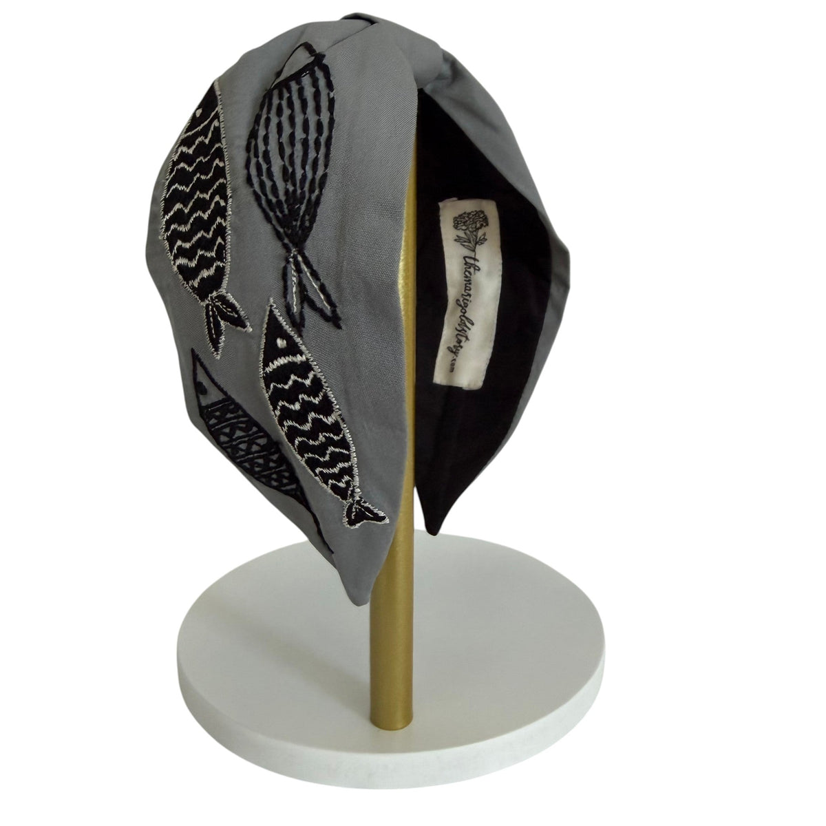 The Marigold Story grey padded headband featuring hand-embroidered black and white abstract fish motifs