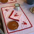 The Marigold Story handcrafted table linen set with pink striped fabric, red lobster embroidery, and red lace borders.