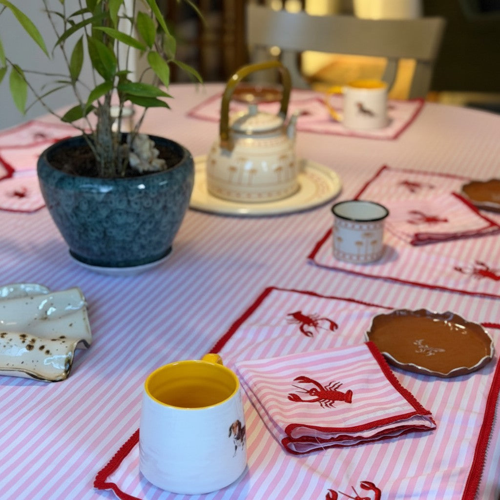 The Marigold Story handcrafted pink striped table linen set with red lobster embroidery and red lace trim on a table