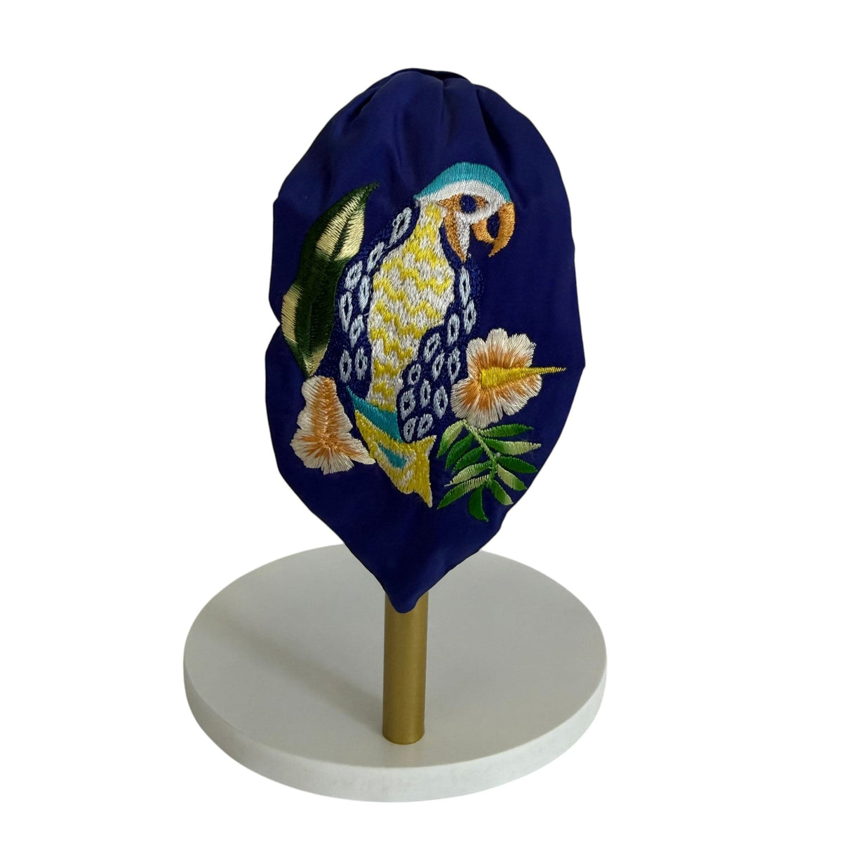 The Marigold Story navy blue padded headband featuring intricate hand-embroidered tropical parrot and floral motifs.