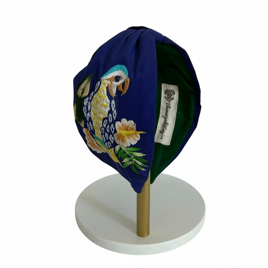 The Marigold Story navy blue padded headband featuring intricate hand-embroidered tropical parrot and floral motifs.