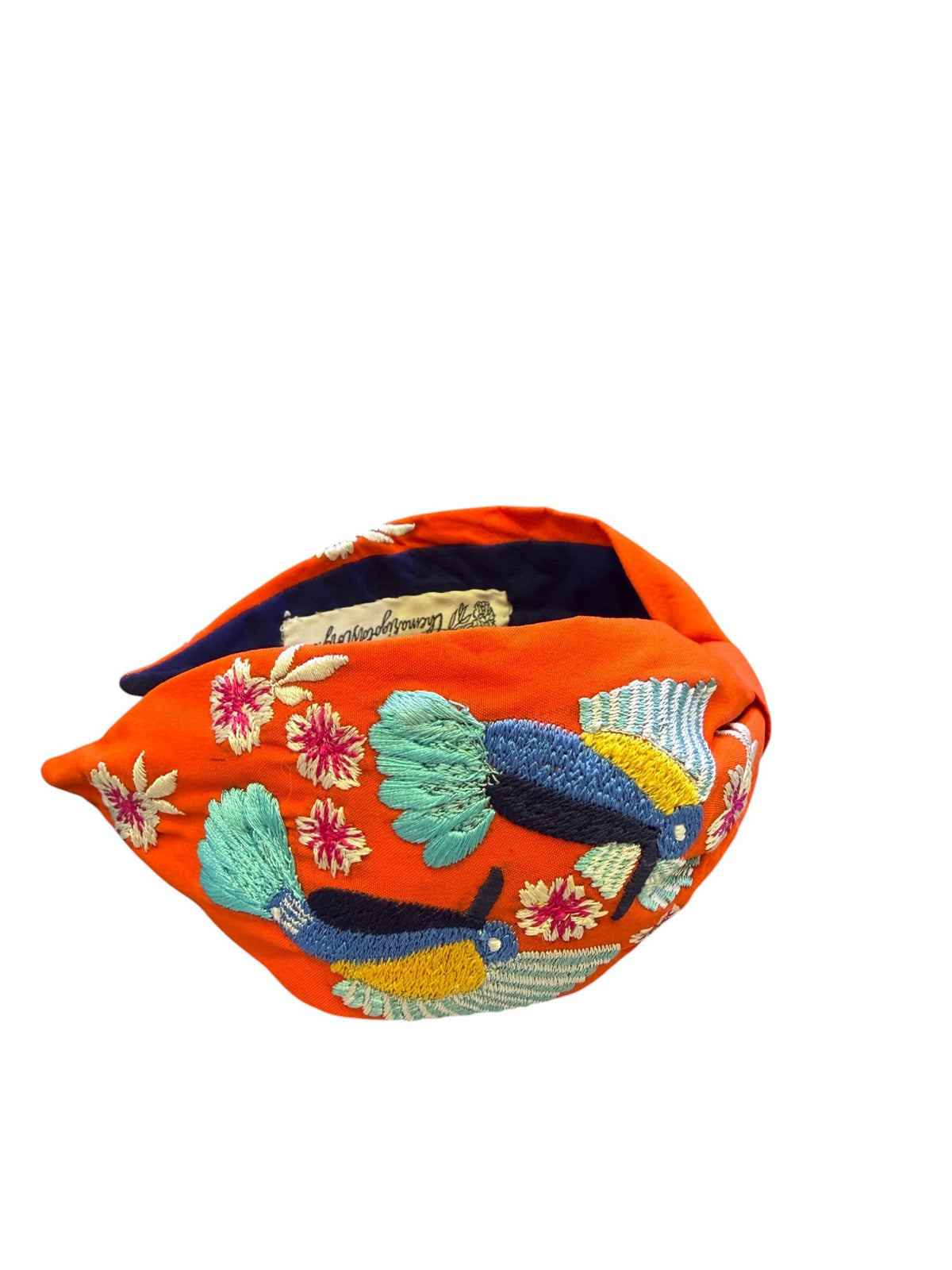 The Marigold Story orange headband featuring hand-embroidered toucans and tropical flowers in vibrant threadwork.