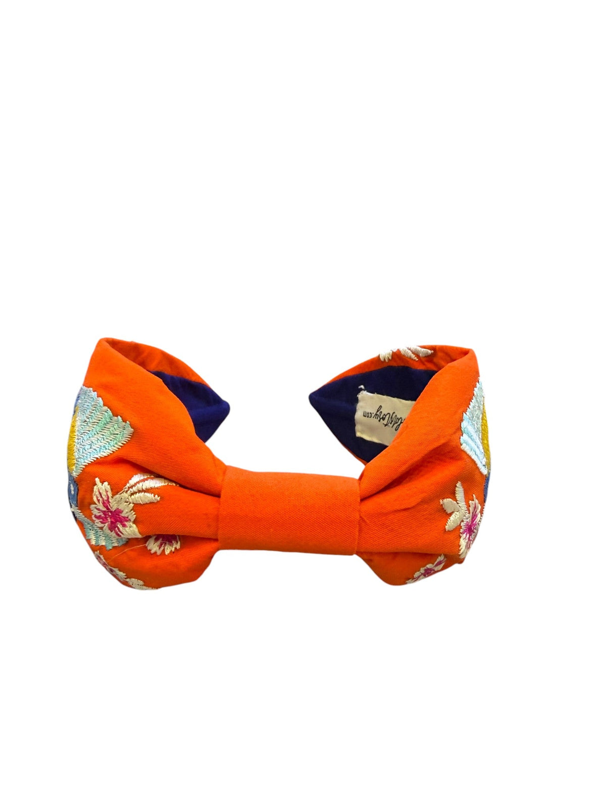 The Marigold Story orange headband featuring hand-embroidered tropical toucans and floral motifs with navy lining.