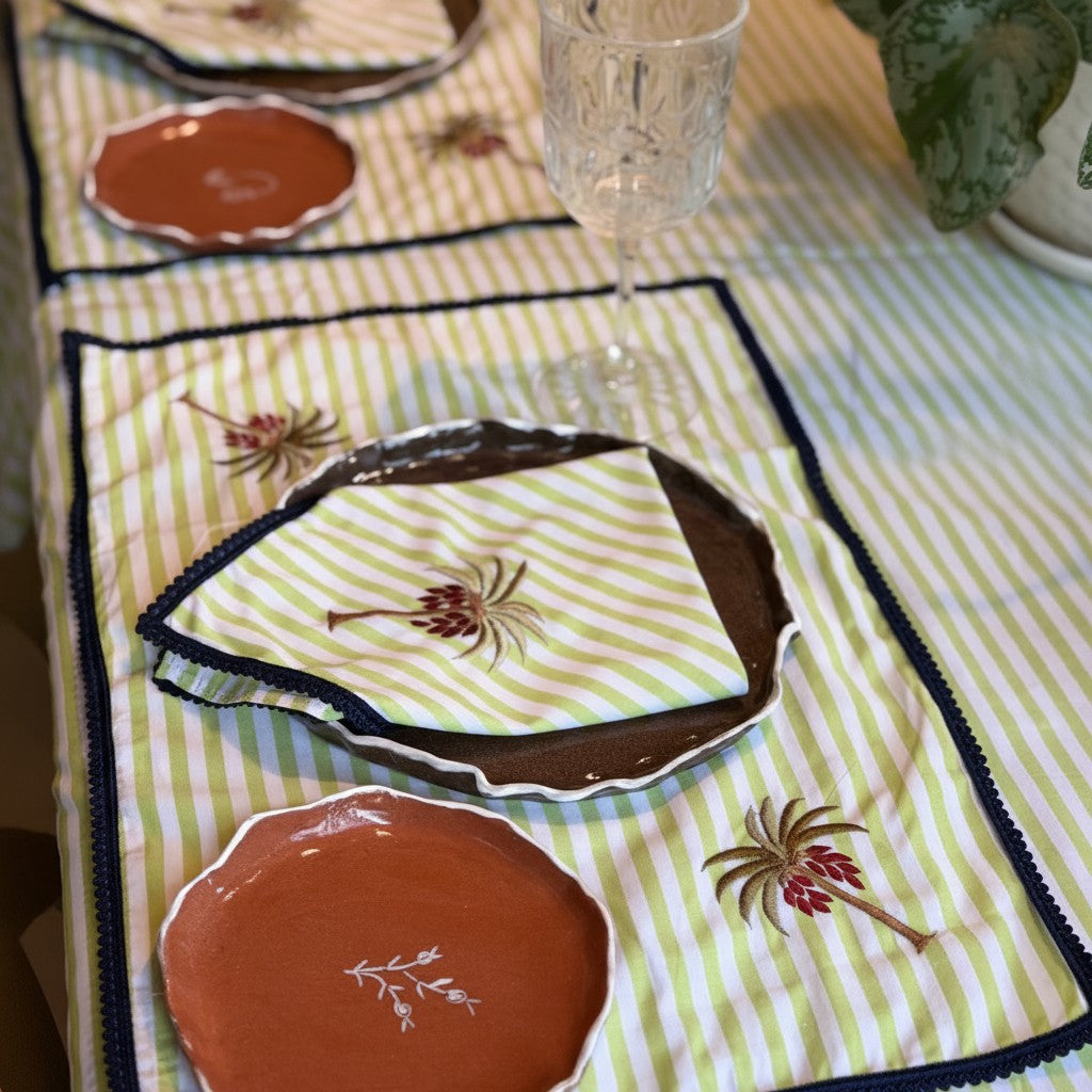 The Marigold Story handcrafted green and white striped table linen set with embroidered palm tree motifs and borders.