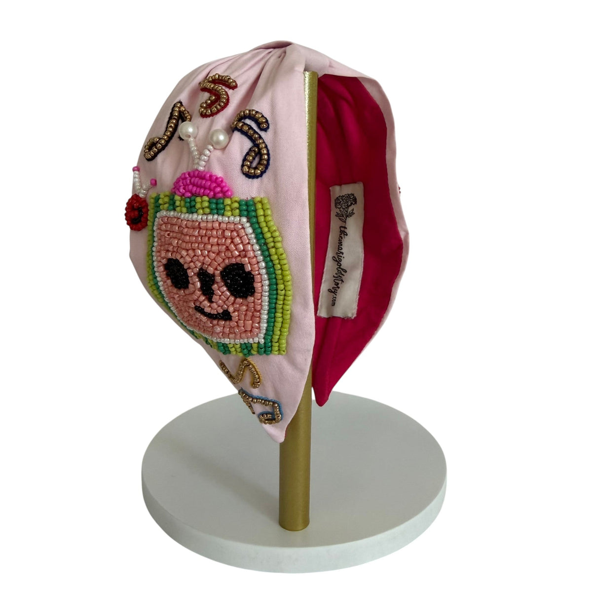 The Marigold Story pink padded headband featuring a handcrafted beaded watermelon character and musical note accents.