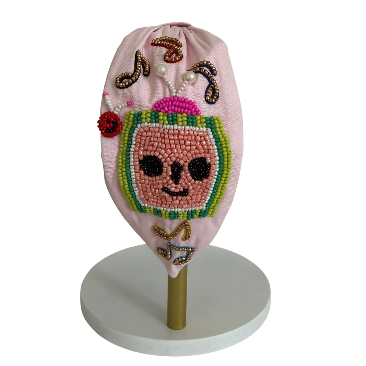 The Marigold Story handcrafted pink padded headband featuring a beaded watermelon character and musical note accents.