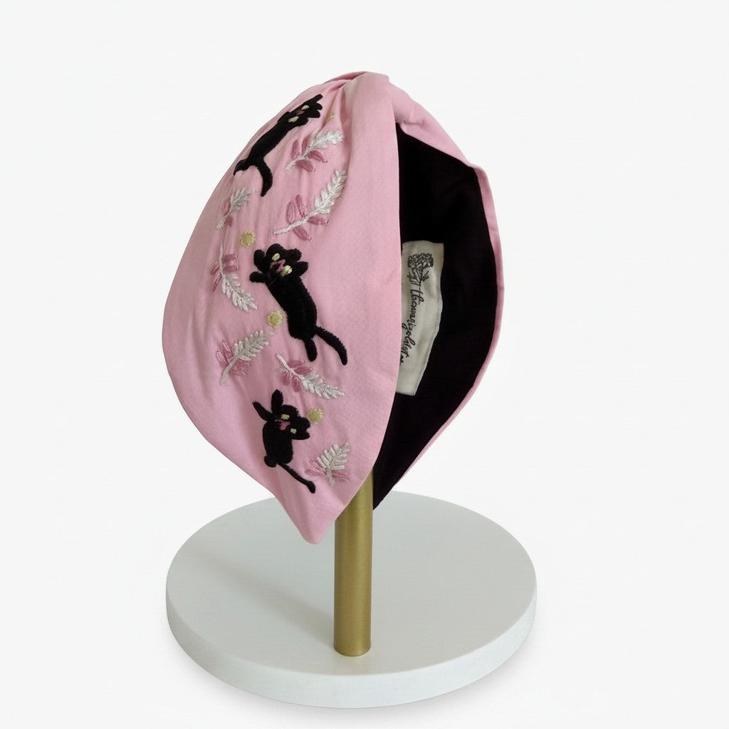 The Marigold Story pink padded headband with hand-embroidered black cats and silver botanical fern motifs.