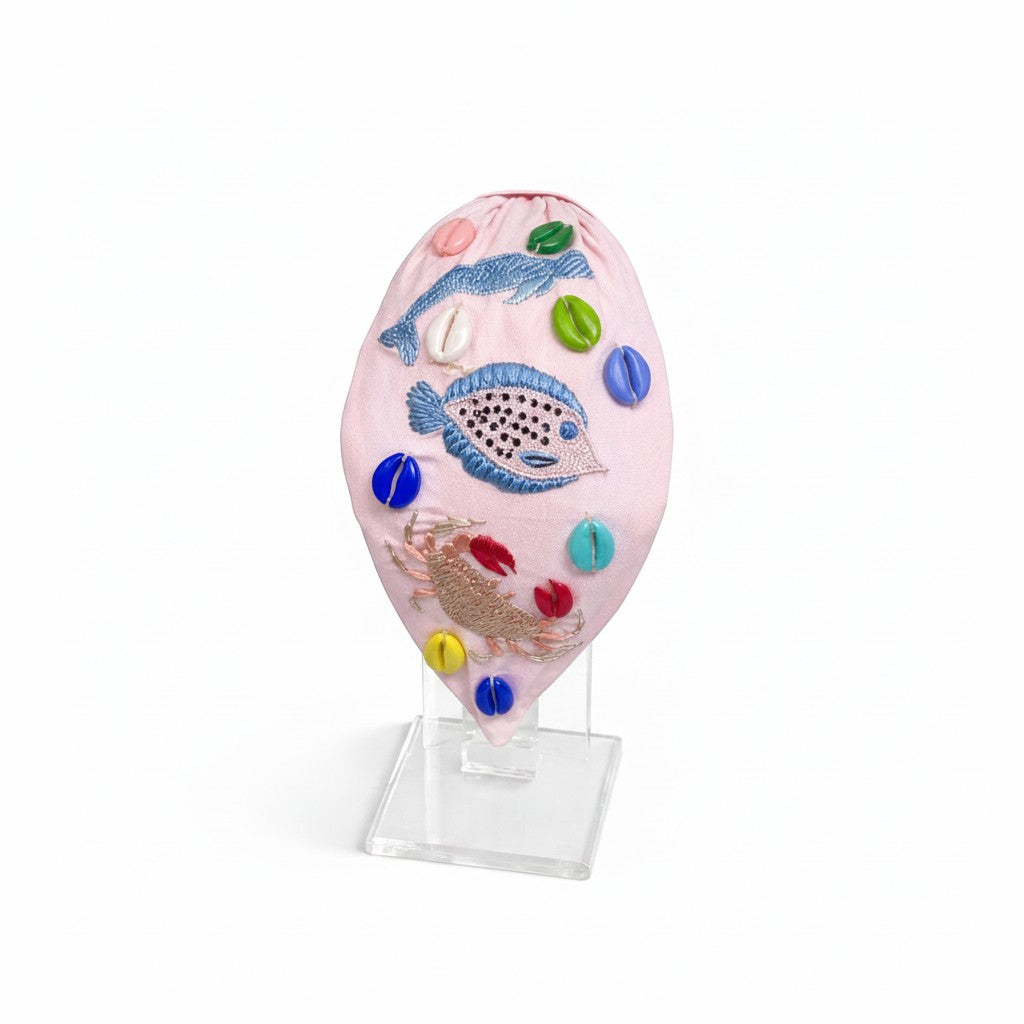 The Marigold Story pink headband featuring hand-embroidered fish, crab, and seashell bead embellishments.