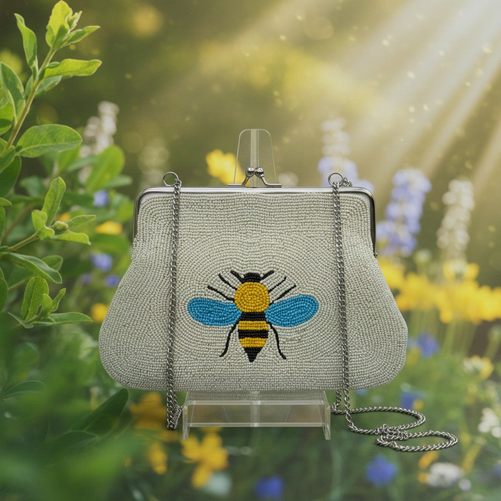 The Marigold Story white beaded sling bag featuring a vibrant bee motif with a metal frame and chain strap.