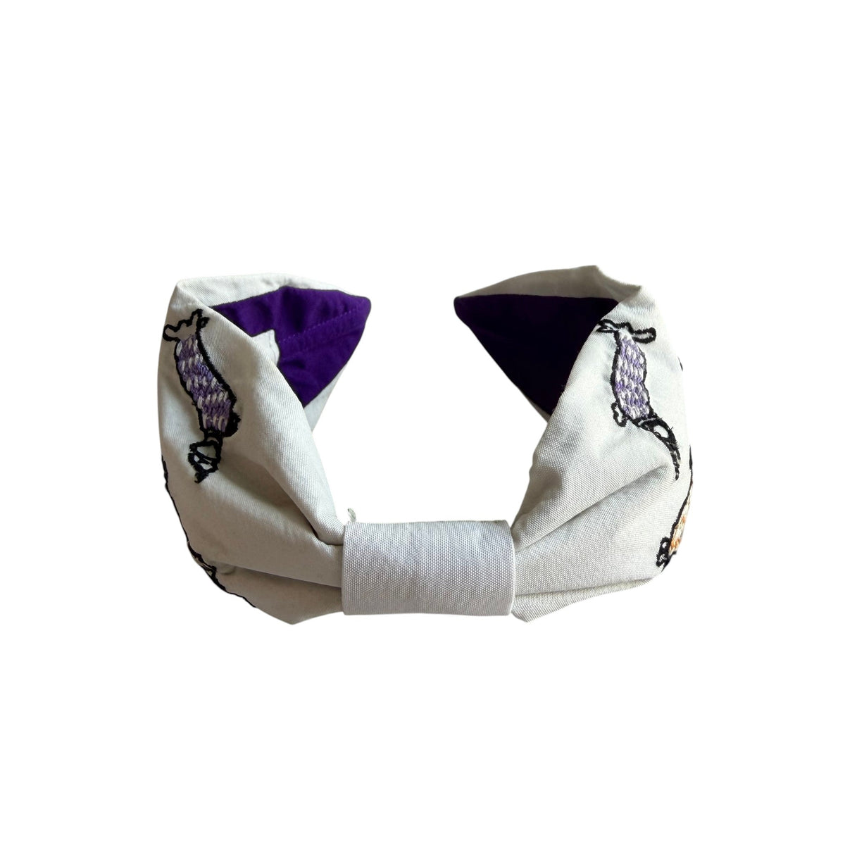 The Marigold Story white headband featuring hand-embroidered dachshunds in purple, blush pink, and burnt orange.